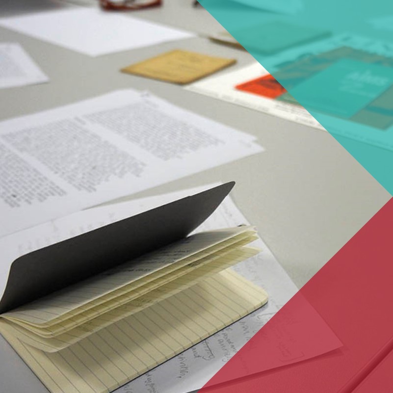 A photograph of a table with various papers, posters, notebooks and printouts scattered around